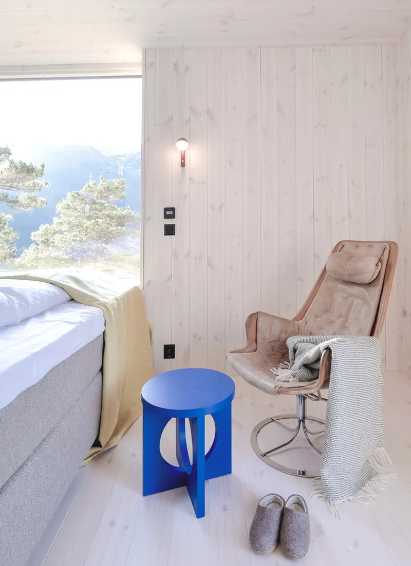 Bedroom corner with wide horizontal window, pale wood cladding and a blue cutout side table