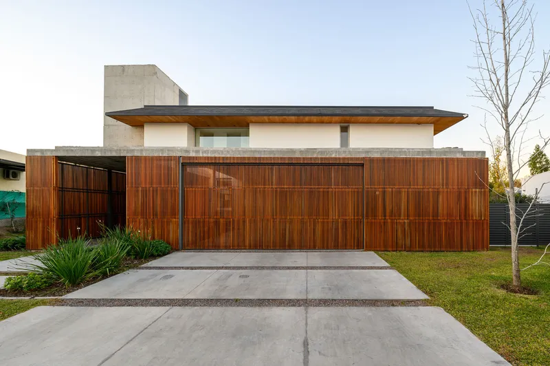 Street view of the vertical wood slat garage door and fence with planted beds and lawn