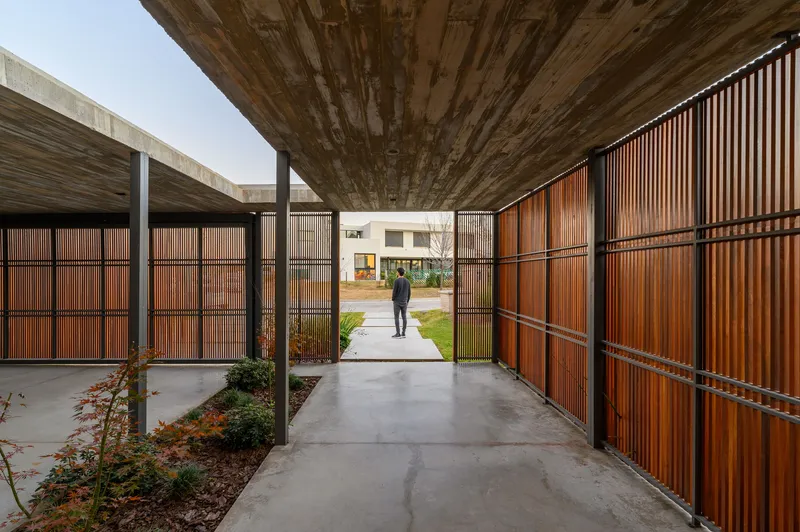 Covered walkway with timber soffit and wood slat screen walls framing a figure in the courtyard