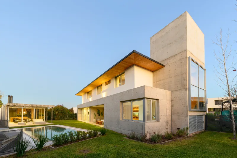 Rear facade showing concrete volumes and timber soffit alongside a reflecting pool at dusk