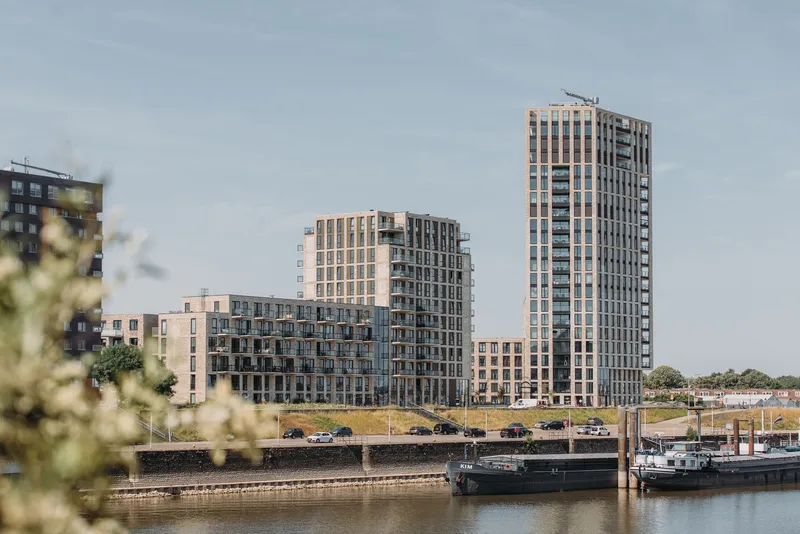 Cluster of brick residential towers seen across a canal with moored barges and white flowering branches in the foreground