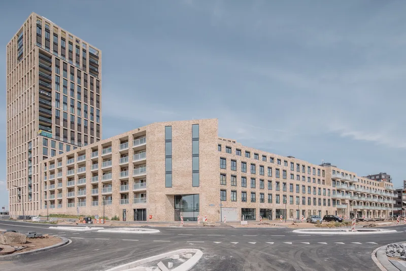 Corner view of the buff brick facade stepping down to a ground-level commercial base at a roundabout