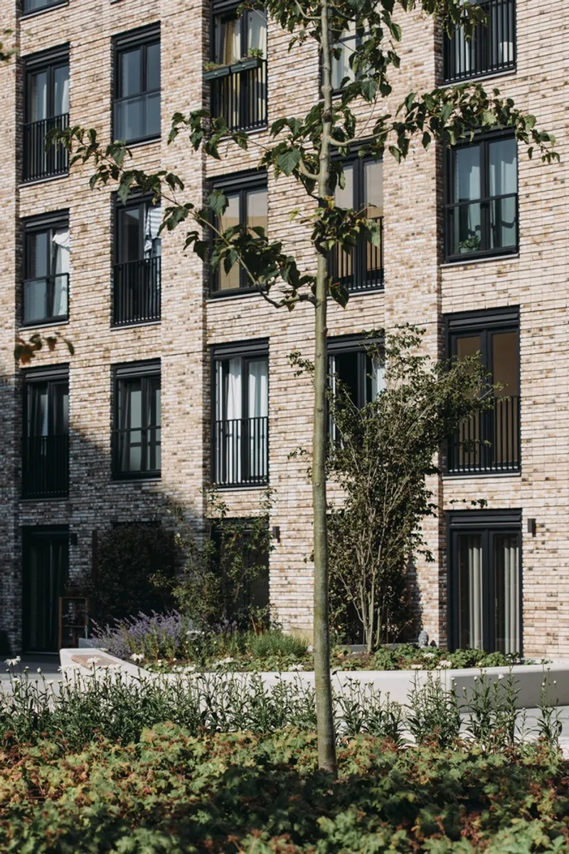 Brick facade with balconies behind a planted bed with lavender and young trees