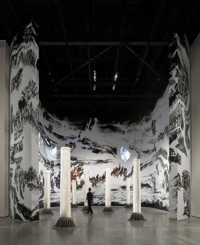 Exhibition space with cylindrical illuminated columns and a figure moving through curved panoramic printed wall panels