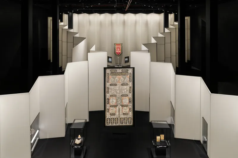 Top-down view of stepped white display platforms arranged symmetrically around a central textile under backlit fabric panels