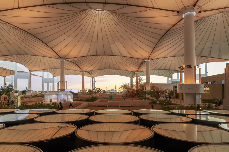 Umbrella-like fabric canopies over a terrace plaza with circular reflecting pools at dusk
