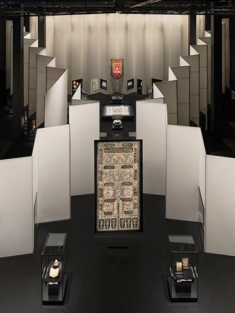 Overhead view of symmetrical white stepped platforms converging toward a central ornate textile on black flooring
