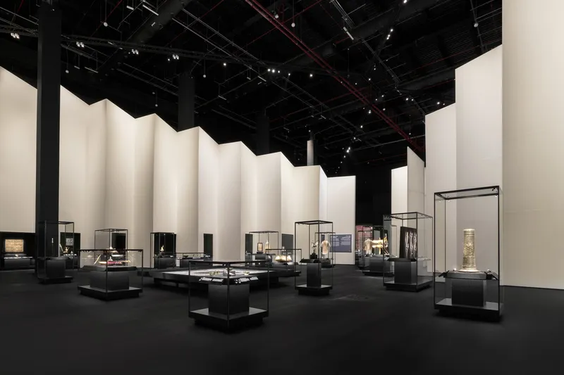 Gallery interior with glass display cases on black plinths arranged before folded cream fabric walls