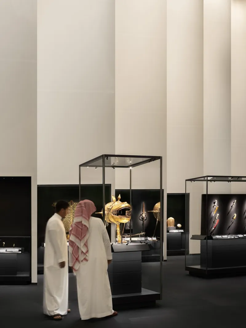 Two visitors in traditional dress viewing artifacts within glass vitrines against tall illuminated panels