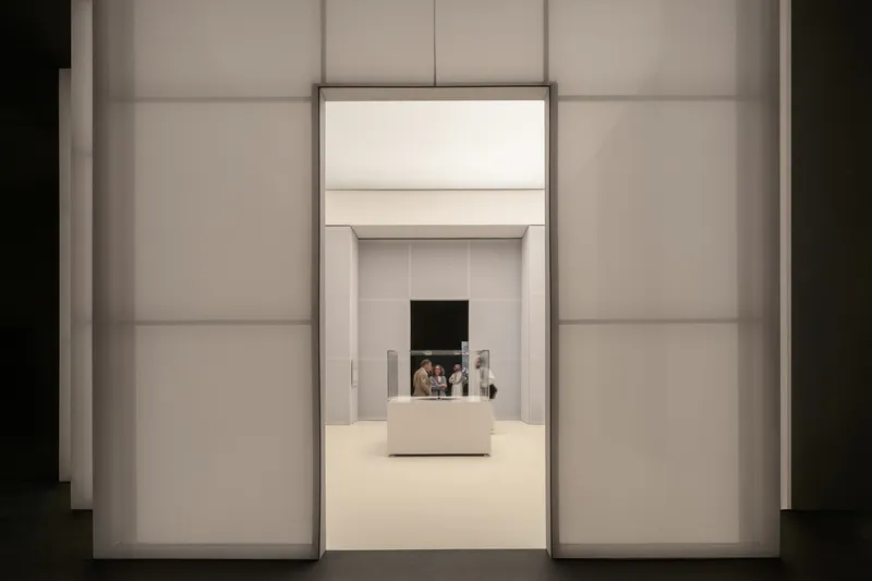 Axial view through illuminated white doorways with visitors visible in the distant gallery beyond