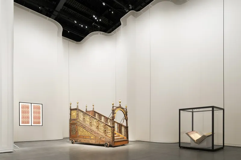 White gallery space with undulating ceiling soffit and exposed black mechanical systems overhead