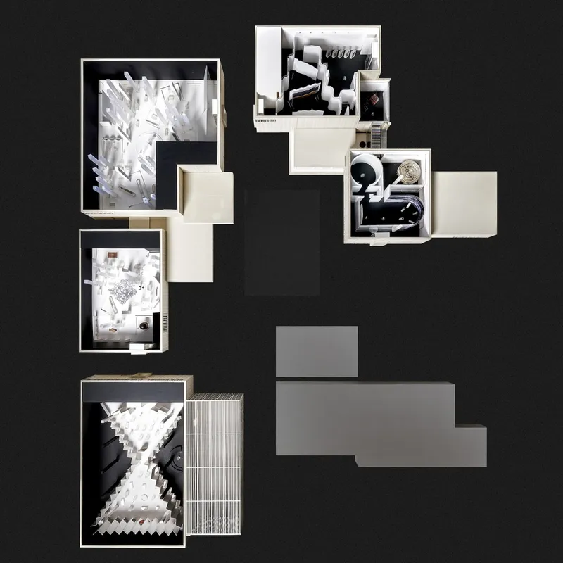 Top-down view of a physical model showing multiple rooms with white paper study models on a black surface