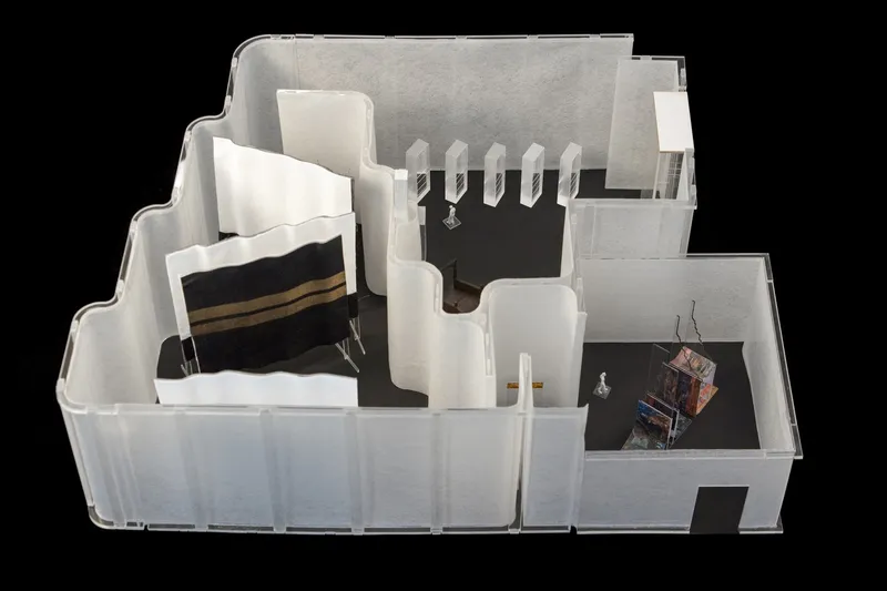 Top-down view of a sectional model showing interior rooms with suspended ceiling elements and material samples
