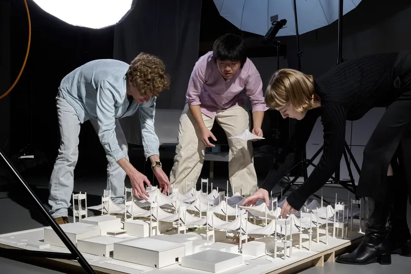Three people arranging white model elements on a table under studio lighting