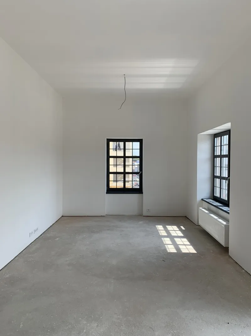 Empty room with concrete floor and two black-framed windows creating grid shadows on the floor