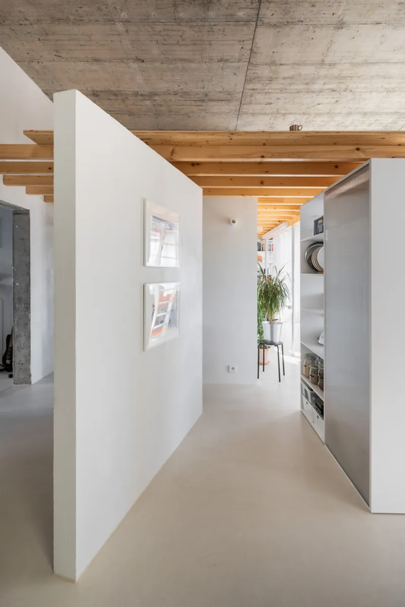 Corridor with freestanding white partition walls and pale resin floor beneath exposed timber beams