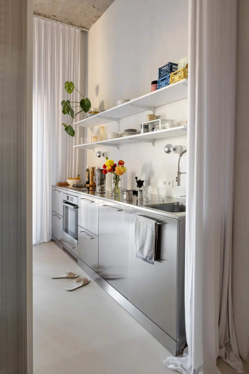 Galley kitchen with stainless steel cabinetry and open shelving framed by sheer white curtains