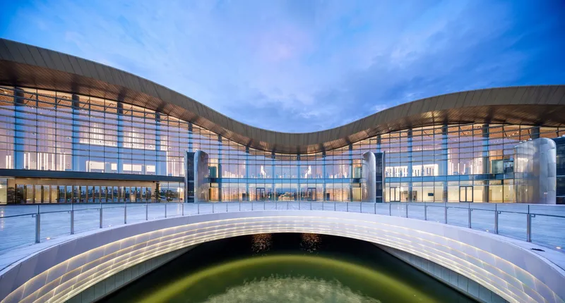 Glazed entrance courtyard with illuminated interiors visible at dusk beneath a cloudy sky