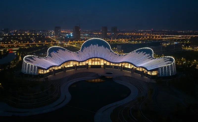 Frontal night view of the illuminated five-lobed ribbed roof above a circular forecourt