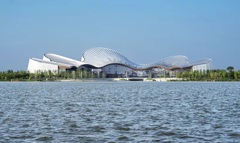 View across the lake showing the rippling white roof forms and glazed base under blue sky