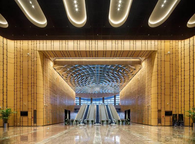 Interior lobby with polished stone floor, timber-clad walls and spiral-patterned ceiling oculus above escalators