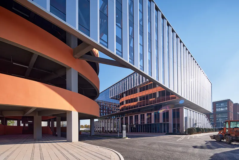 Orange curved structural supports beneath the elevated volume alongside vertical fin cladding
