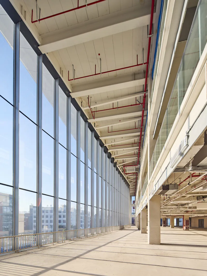 Interior corridor with floor-to-ceiling glazing, exposed ceiling with red piping and concrete beams