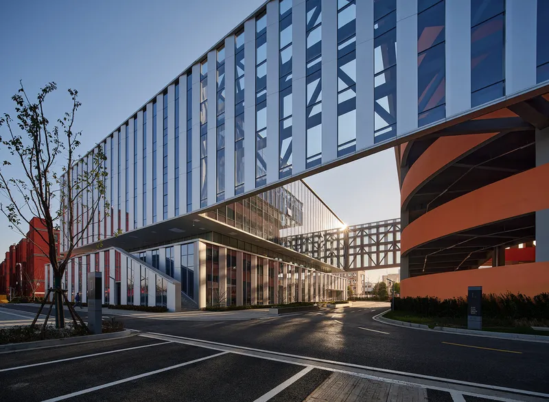 Street-level view showing the cantilevered volume above glass lobby and orange structural elements at sunset