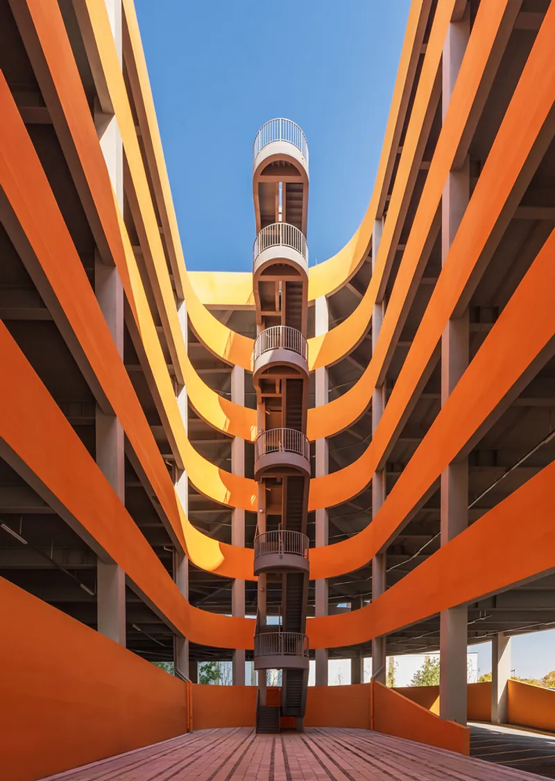 Courtyard view of layered orange balconies wrapping around a central vertical core with cylindrical stair tower