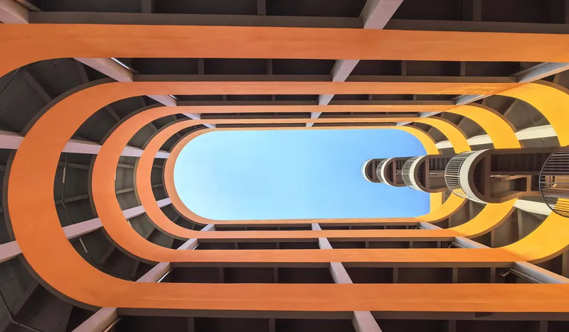 Upward view through the oval parking atrium framing the cylindrical stair tower against blue sky