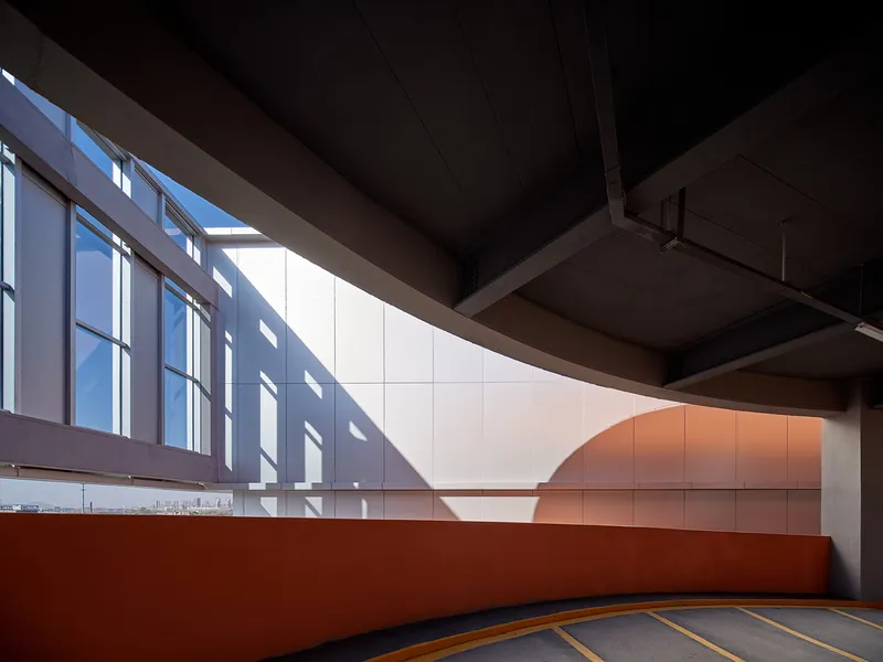 Interior parking ramp with curved wall panels and sunlight through vertical window openings