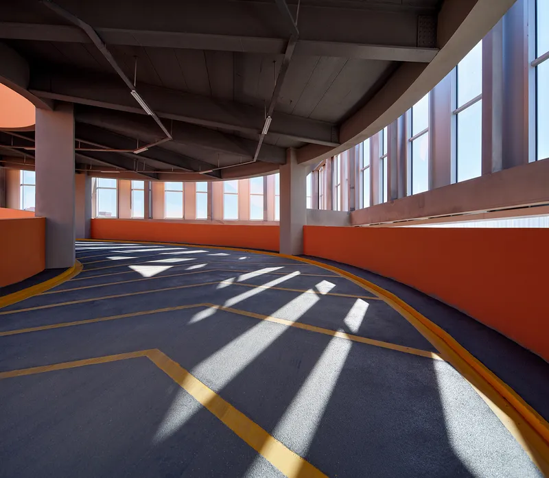 Curving parking level with exposed concrete structure and striped sunlight through vertical screening