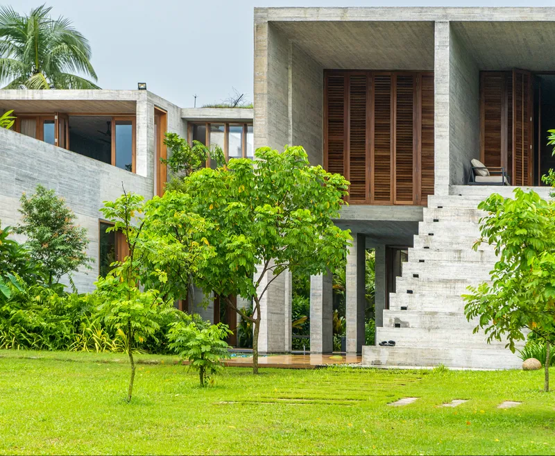 Garden view of the elevated concrete volumes with timber louvers, external staircase and lawn with young trees