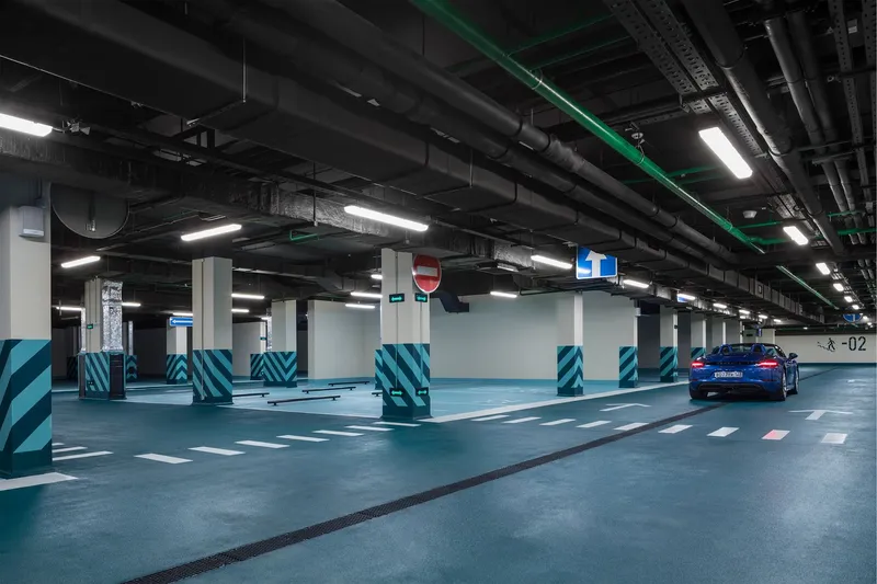 Underground parking garage with exposed ceiling ducts and columns wrapped in diagonal turquoise and black stripes