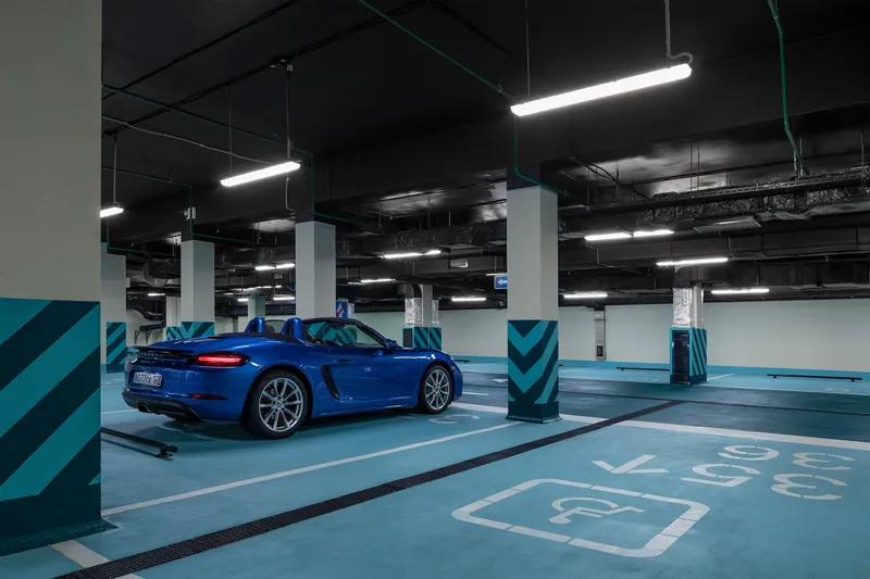 Blue convertible parked in the garage beneath suspended linear lights and green conduit runs