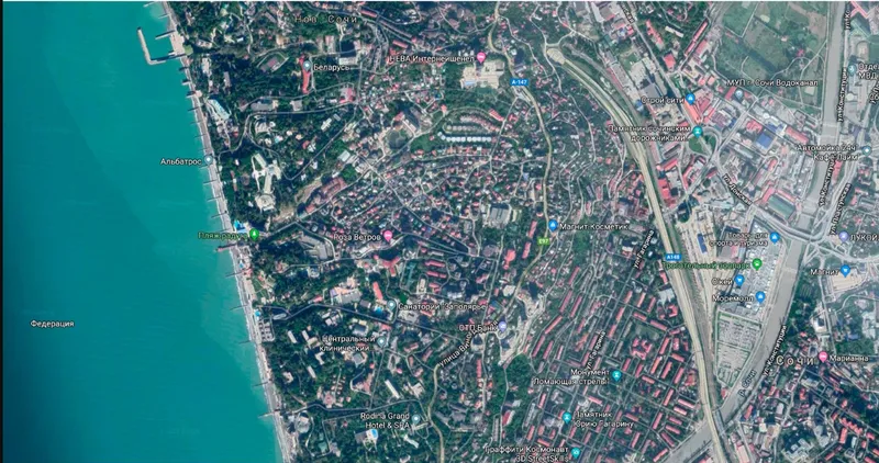 Satellite view showing the building footprint adjacent to wooded neighborhoods and a turquoise sea