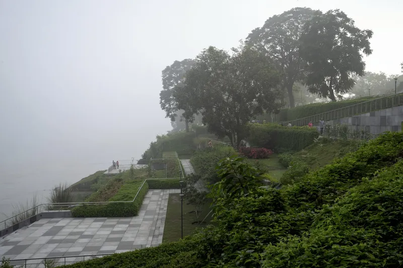 Terraced paved plaza with chequered stone pattern and planted embankments descending toward the misty waterfront
