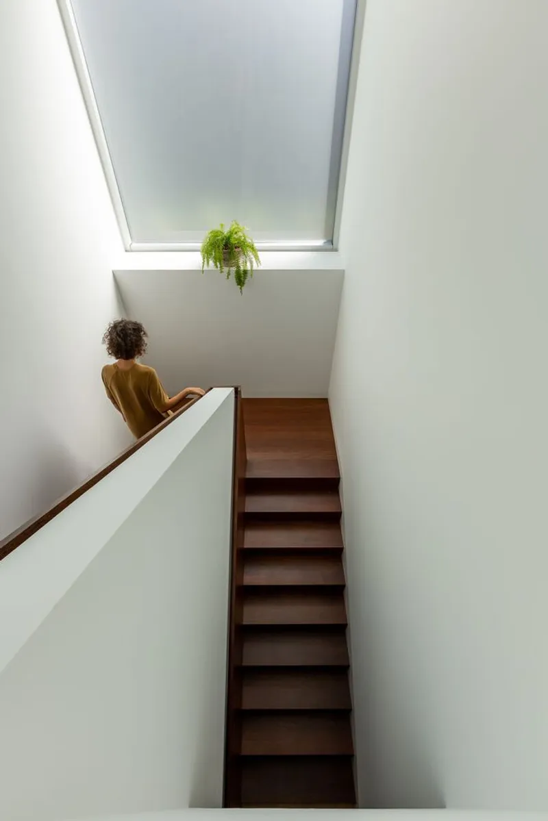 Wooden staircase rising to a skylight with hanging fern and person seated at the landing