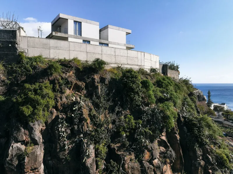 White concrete volumes perched atop a rugged volcanic cliff with ocean horizon visible beyond