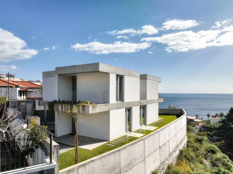 Tiered concrete retaining walls with planted grass steps descending toward the coastal view below