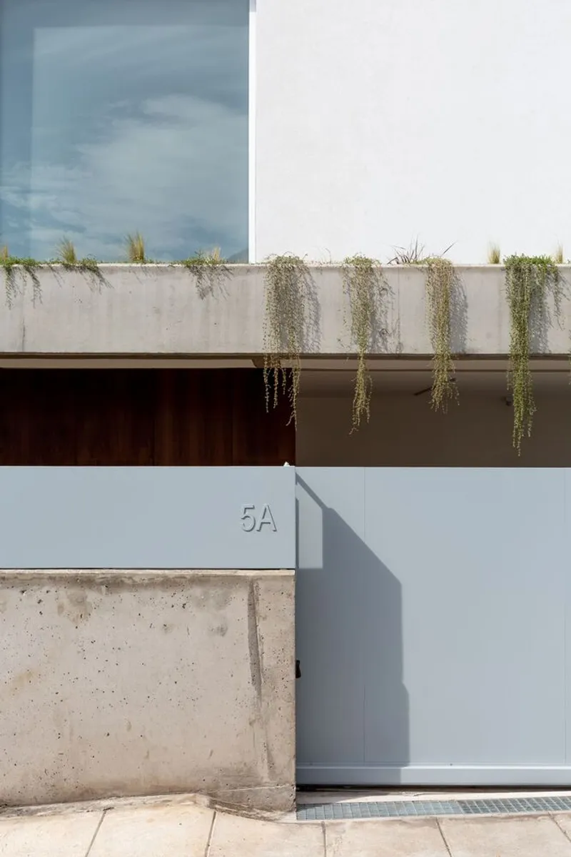 Street facade with concrete planter box trailing vegetation above a metal garage door under storm clouds