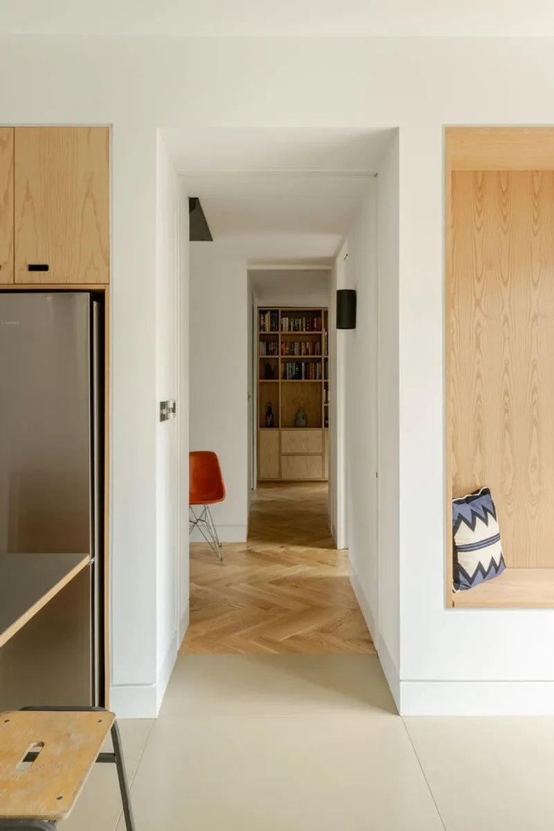Corridor view from polished concrete floor through white walls toward herringbone timber and built-in bookshelf