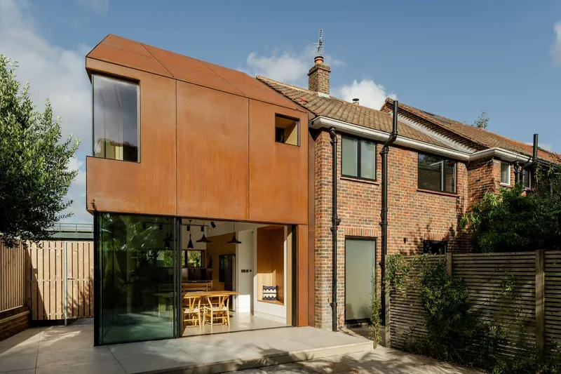Rear elevation showing the cantilevered corten volume above floor-to-ceiling glazing and brick terrace