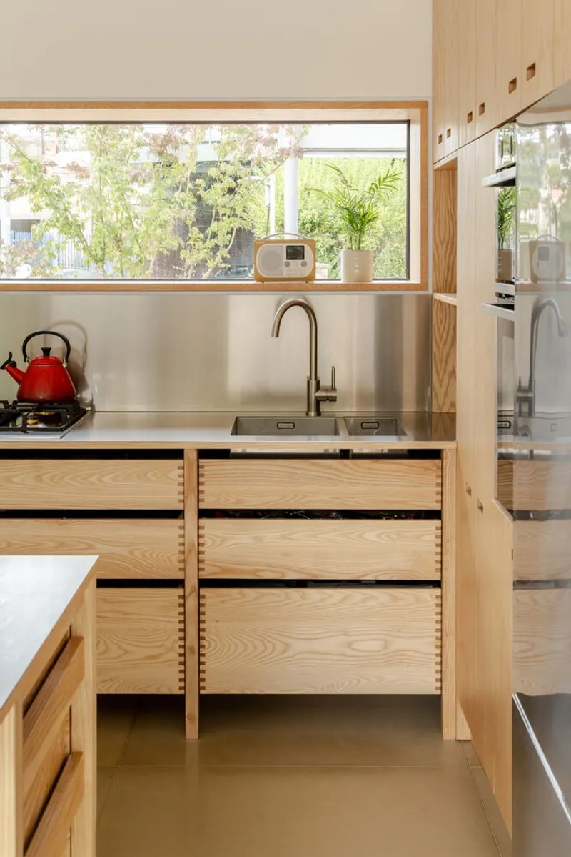 Kitchen counter with stainless steel splashback and timber drawers opened to reveal interior storage organization