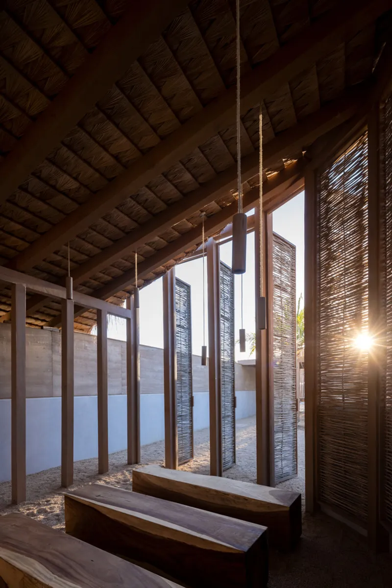 Timber bench beneath exposed rafters framed by vertical screens with late afternoon sunlight streaming through