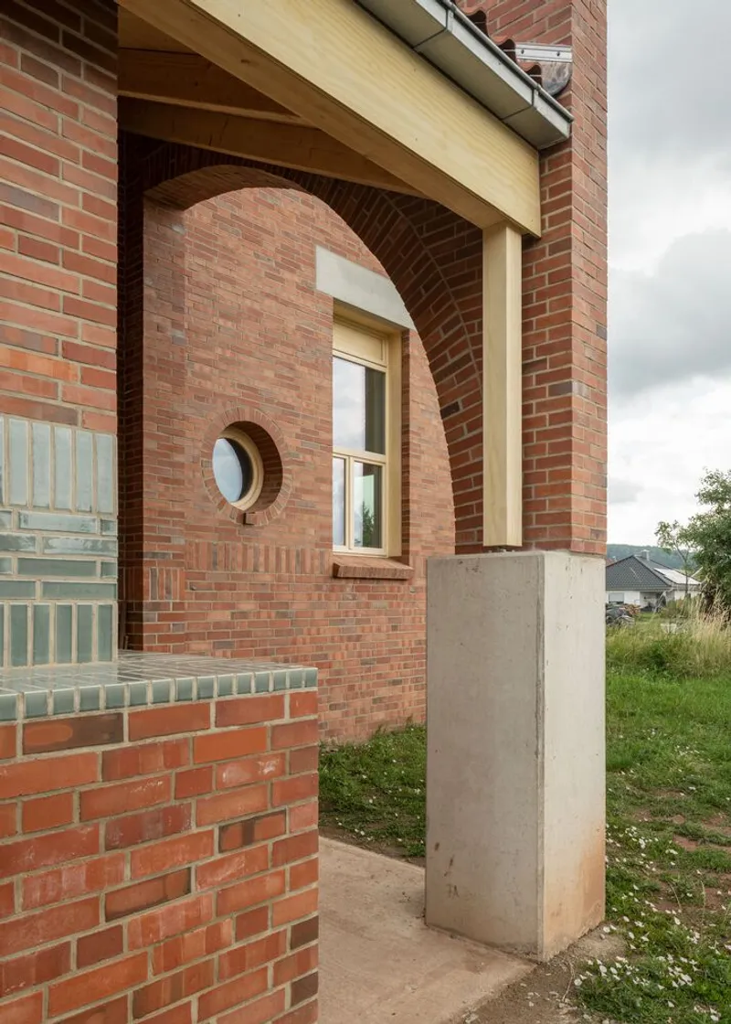 Arched brick opening with circular window and timber fascia detail supported by a concrete plinth