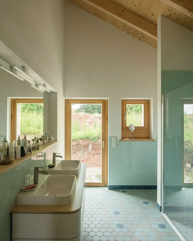 Bathroom with double vanity, hexagonal tile floor, and pale green vertical tile wainscoting under exposed rafters