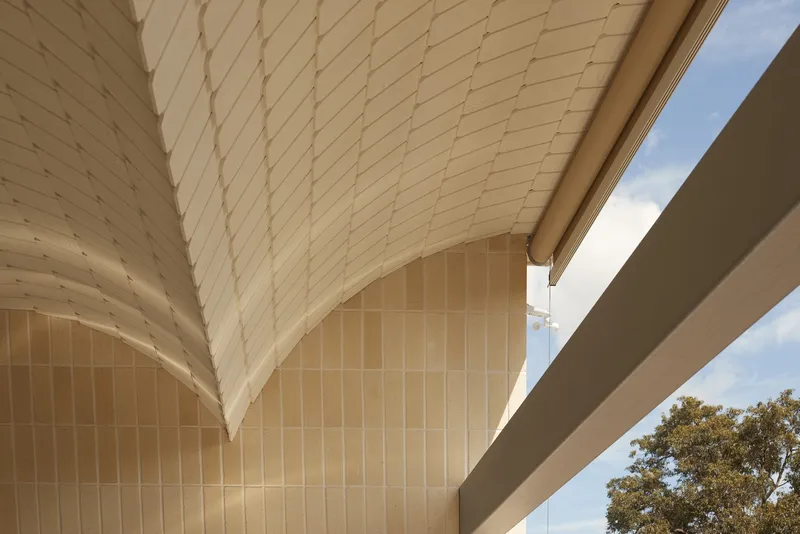 Upward view of cream tiled soffit meeting curved wall under a blue afternoon sky