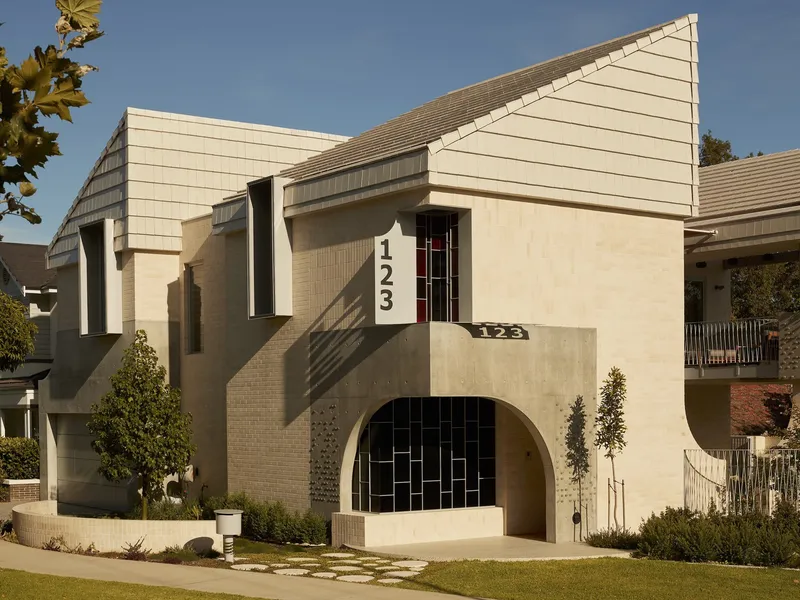 Street facade with stepped roofline, arched entry with black tile and address numbers in afternoon light