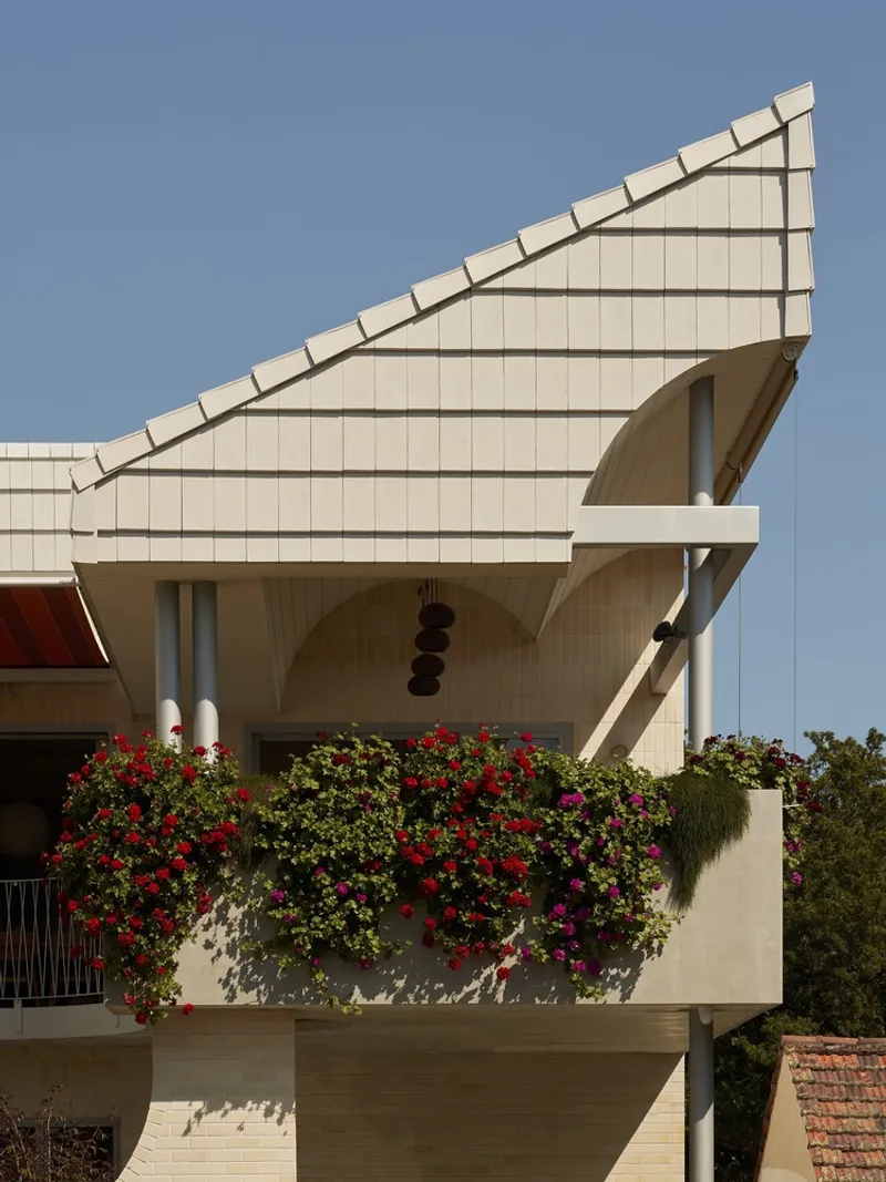 Balcony planter overflowing with red and purple flowers beneath the angular tiled roof edge